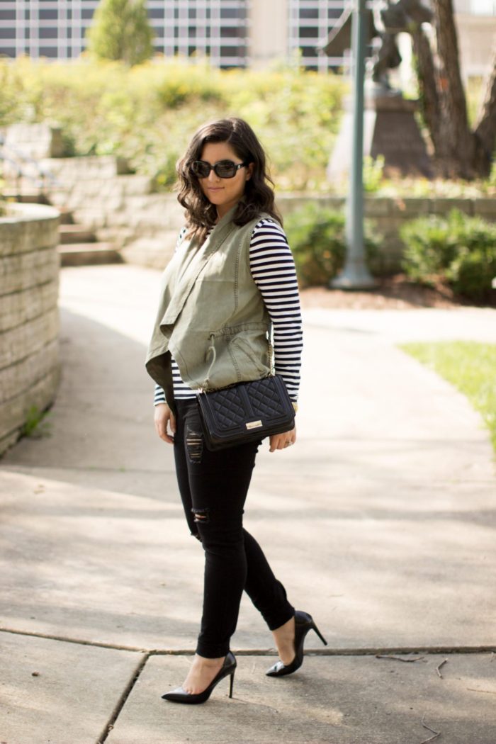 how to style a green utility vest, striped top, black skinny jeans, distressed black jeans, black quilted crossbody handbag, fall outfit idea, casual fall outfit